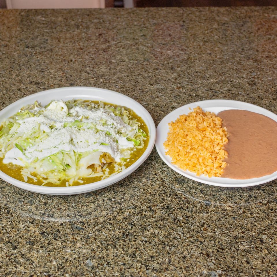 Mexican meal featuring a green-sauced dish topped with lettuce, cream, and cheese, served with Spanish rice and refried beans.