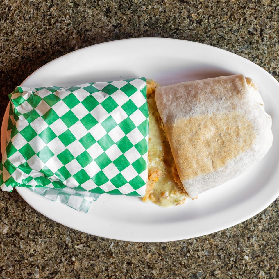 Two wrapped burritos on a white plate, one partially covered in green-and-white checkered paper, on a granite countertop.