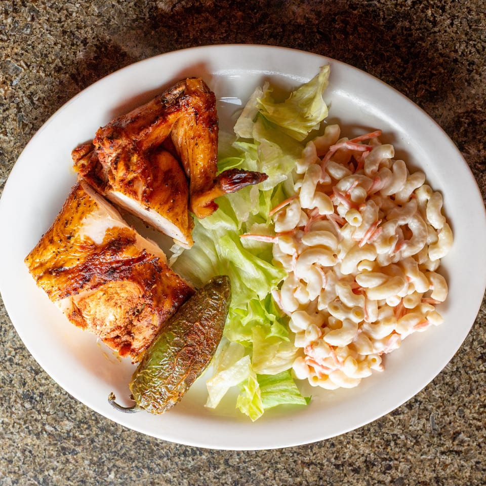 Plate of grilled chicken with lettuce, creamy macaroni salad, and grilled vegetables on a white dish.