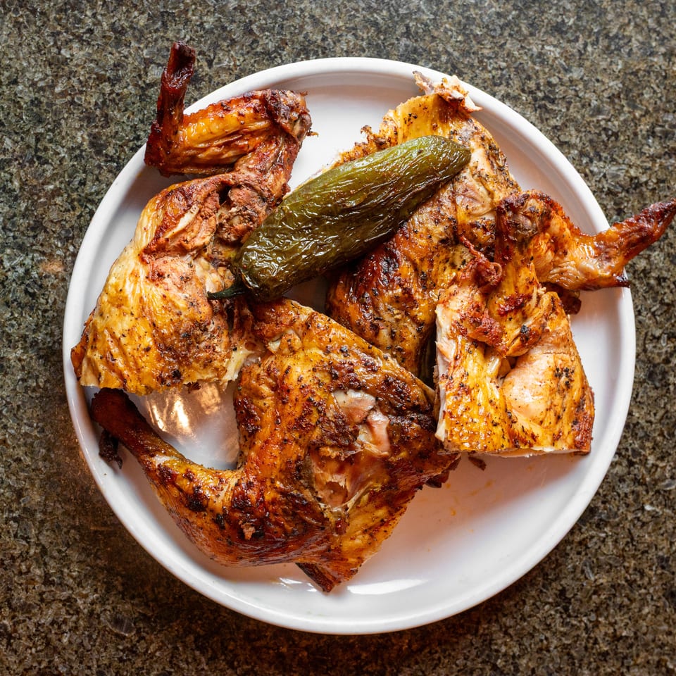 Plate of seasoned roasted chicken pieces topped with a grilled green pepper on a granite countertop.