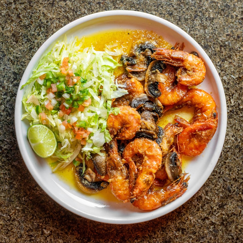 Plate of sautéed shrimp and mushrooms with shredded lettuce, pico de gallo, lime, and yellow sauce.