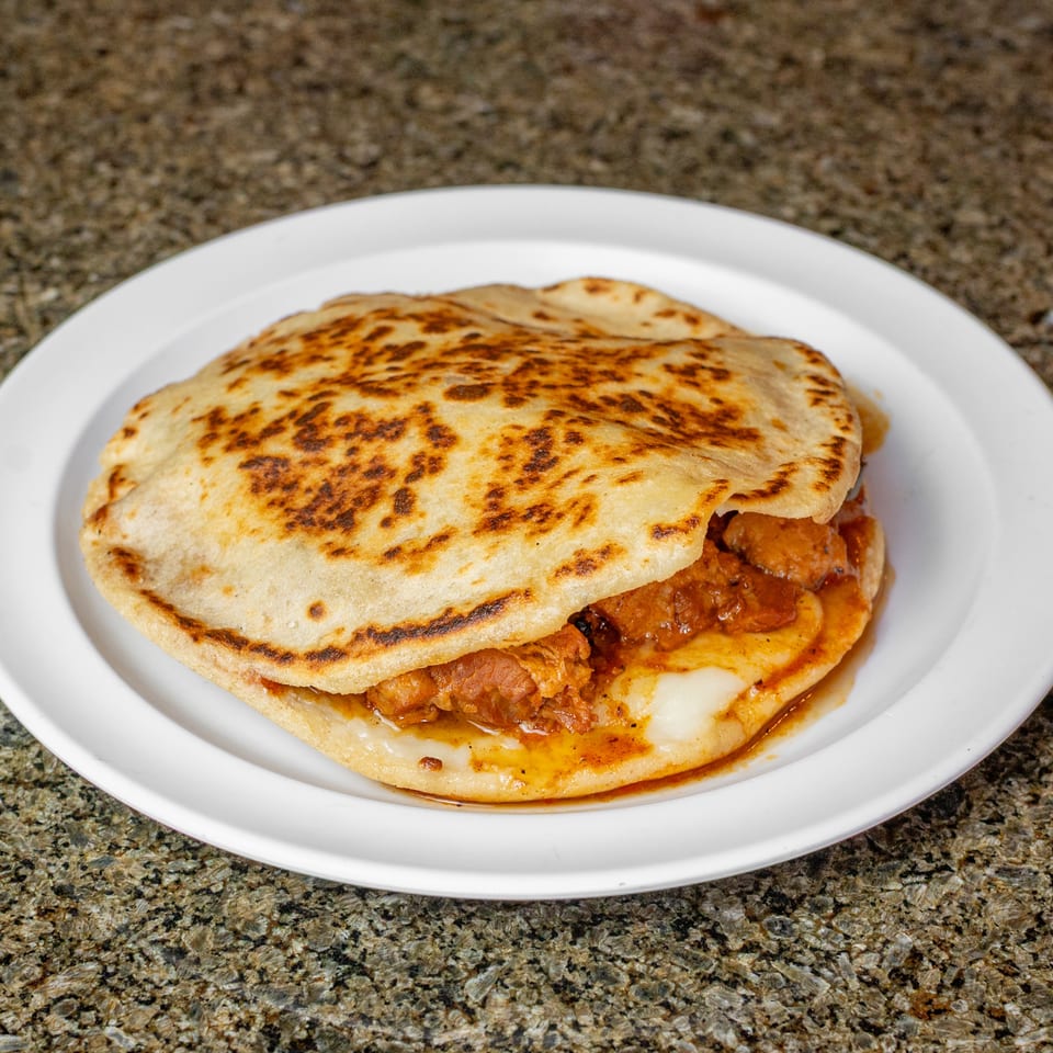 Grilled stuffed flatbread with melted cheese and savory filling on a white plate atop a granite countertop.