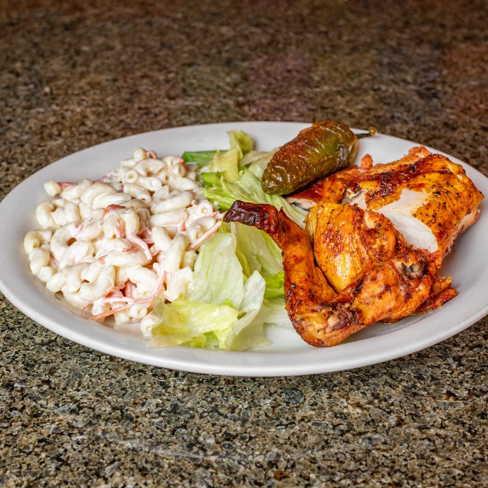 Plate of grilled chicken with creamy macaroni salad, lettuce, roasted pepper, and grilled vegetables on a granite countertop.