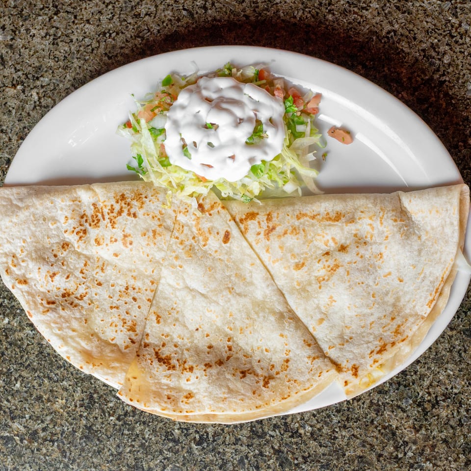 Plate of grilled flour tortillas served with shredded lettuce, diced tomatoes, peppers, and creamy white sauce.