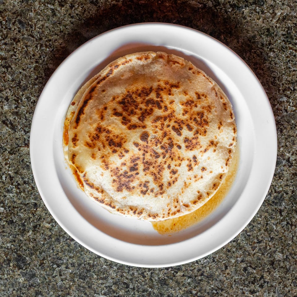 Golden-brown stuffed flatbread with charred spots served on a white plate over a granite countertop.