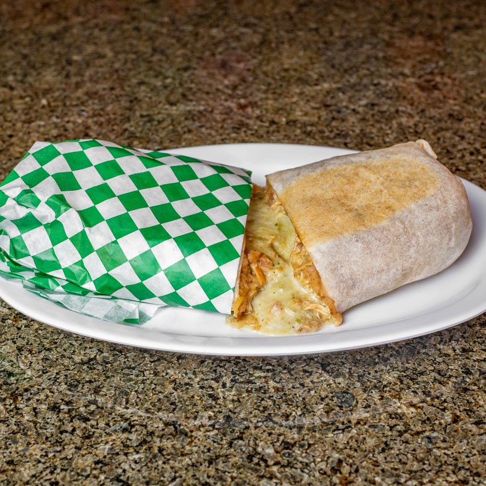 Cheesy chicken burrito partially wrapped in green-and-white checkered paper on a white plate.